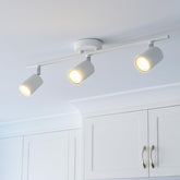 Three ceiling-mounted spotlights on a white ceiling with white cabinets below.