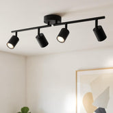 Black ceiling light fixture with four spotlights on a white wall background