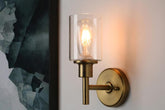 Brass wall sconce with clear glass shade on a white wall.