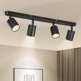Black ceiling light fixture with four spotlights on a beige ceiling.