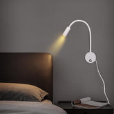 Wall-mounted reading lamp on a dark wall next to a bed