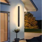 Modern outdoor wall light fixture on a house exterior with a garden view.