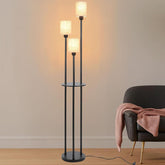 Black floor lamp with three lampshades in a room with a chair and pink blanket.