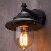Vintage-style wall light fixture with clear glass shade on a concrete wall.