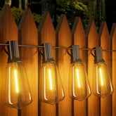 String of illuminated light bulbs hanging against a wooden fence at night.