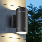 Black outdoor wall light fixture on a concrete wall with blurred trees in the background