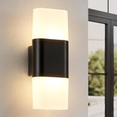 Modern outdoor wall light fixture on a neutral wall with a blurred window view in the background.