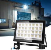 LED flood light with visible brand logo in front of a warehouse at night.