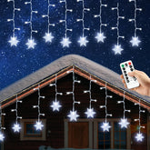 Snowflake string lights on a house exterior with a remote control held by a hand.