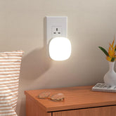 Wall-mounted night light on a beige wall above a wooden surface with a vase and glasses.