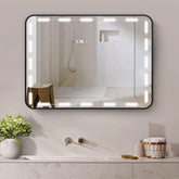 Bathroom mirror with lights reflecting a shower area, next to a sink and decorative items.