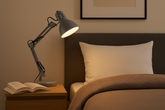 Bedroom scene with a lamp on a nightstand next to a bed with a pillow.