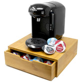 Black coffee machine with a wooden stand holding coffee pods on a white background