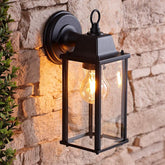 Black outdoor wall lantern with a lit bulb attached to a stone wall.