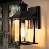 Black outdoor wall light fixture with clear glass shade on a wall.
