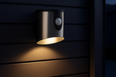 Black outdoor wall light fixture with motion sensor on a dark wooden surface