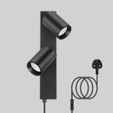 Black wall-mounted light fixture with two cylindrical lights and a cable on a gray background