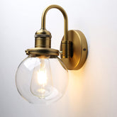 Brass wall-mounted light fixture with a clear glass shade on a white background