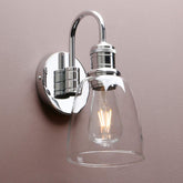 Chrome wall-mounted light fixture with clear glass shade on a beige background