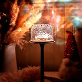 Decorative glass lamp on a stand with pampas grass and colorful lights in the background