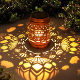 Decorative lantern casting intricate shadows on a ground surface with greenery in the background.
