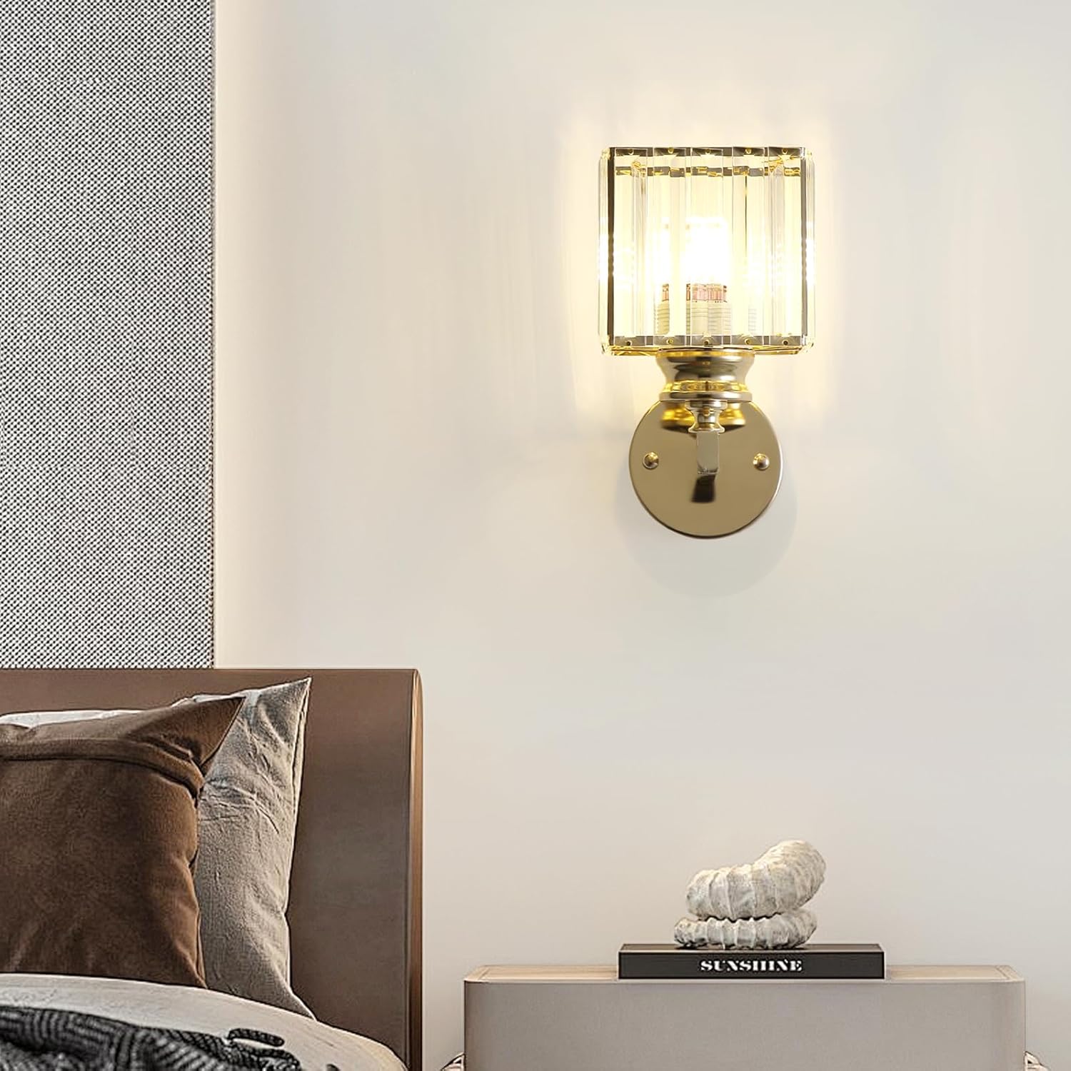 Gold wall sconce with glass shade on a white wall above a bed.