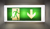 Green emergency exit sign with running person and downward arrow on a dark background