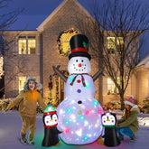 Inflatable snowman with lights and penguins in front of a decorated house at night
