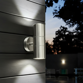 Metallic outdoor wall light fixture on a wooden surface with a night-time background.
