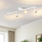 Modern ceiling light fixture with four lights in a room with a window and plants.