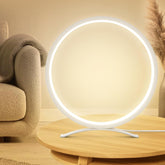 Modern round table lamp on a wooden surface with a beige sofa and decorative plant in the background.