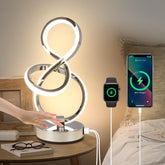 Modern table lamp with smartphone and smartwatch charging on a bedside table.
