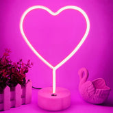 Neon heart-shaped light on a pink base with decorative elements against a pink background