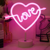 Neon light shaped like a heart with the word 'love' inside, on a pink background.