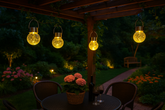 Outdoor patio with hanging solar lights, table, and flowers at night.