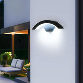 Outdoor wall light fixture on a white wall with a garden and lounge chair in the background.