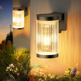 Outdoor wall lights with glass cover on a wall, surrounded by plants and flowers.
