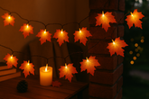 String lights shaped like leaves with a candle on a wooden surface.