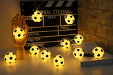 String lights shaped like soccer balls in front of a clapperboard with 'Universal Studios' branding.