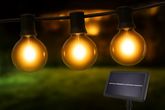 Three illuminated light bulbs on a string with a solar panel in the background.