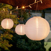 Three paper lanterns hanging outdoors with string lights against a natural background