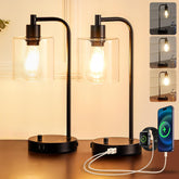 Two black table lamps with glass shades on a wooden surface, one lamp is charging a smartphone.