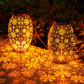Two decorative solar lanterns with floral patterns casting light on a ground surface.