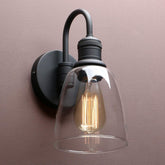 Wall-mounted light fixture with clear glass shade and black metal finish on a beige wall.