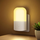 Wall-mounted night light emitting a warm glow on a wall with a plant in the corner.