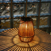Wicker lantern casting a warm glow on a textured surface with a glass block wall in the background.