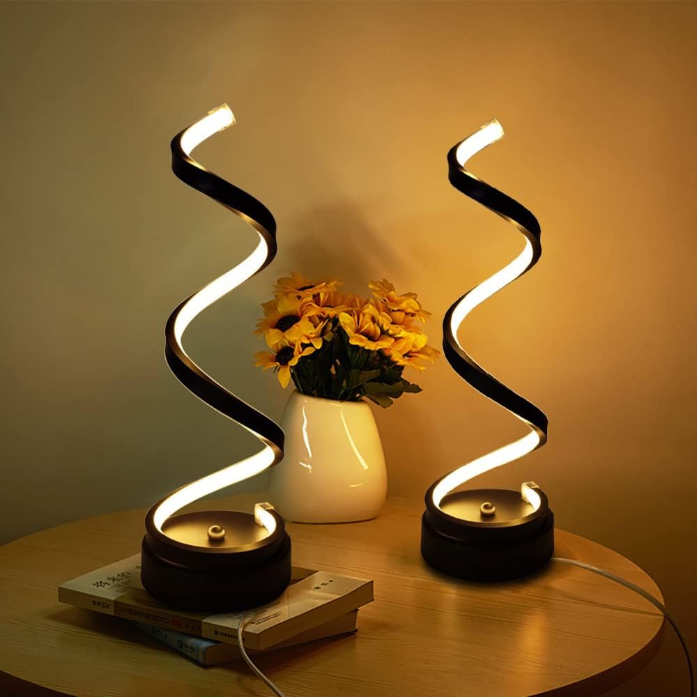 Two spiral LED lamps on a wooden surface with a vase of flowers in the background.