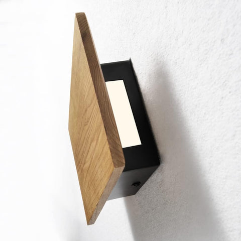 Wall-mounted light fixture with wooden panel and black frame on a white wall