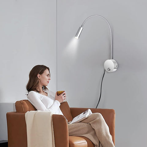 Woman sitting in a brown armchair with a white wall lamp above her