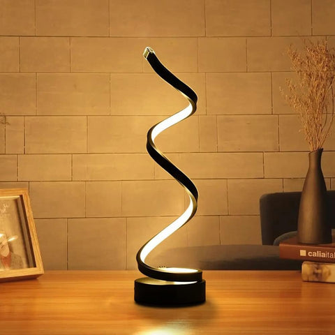 Spiral table lamp on a wooden surface with a warm-toned wall in the background